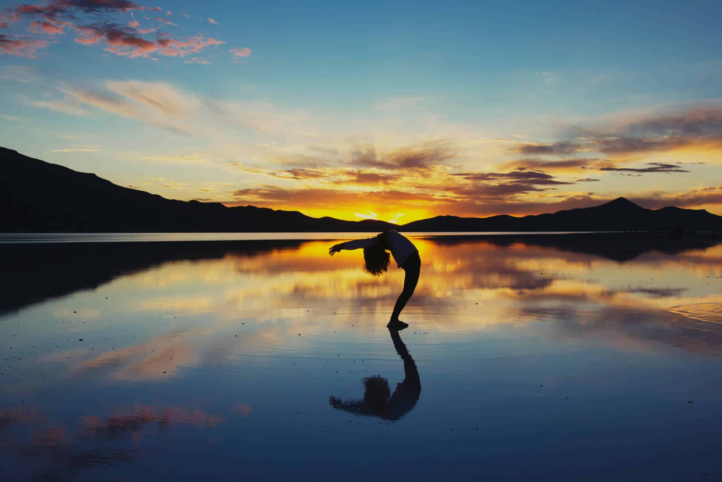 yogi doing a backbend on a glass-like lake at sunset